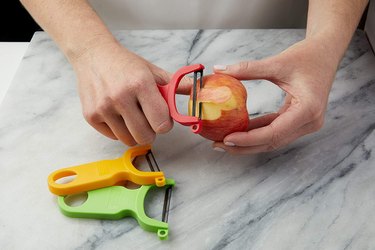 Kuhn Rikon peeler being used on a fruit, over a marble slab