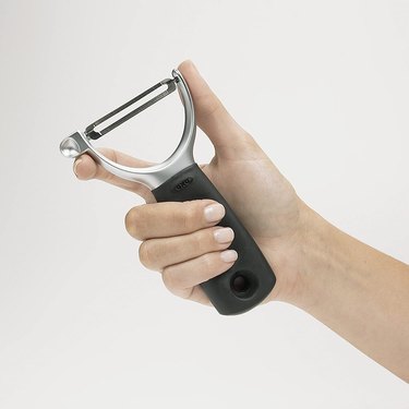 Hand holding an OXO Y-peeler against a grey background