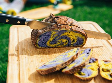 Knife slices a loaf of purple and yellow sourdough bread