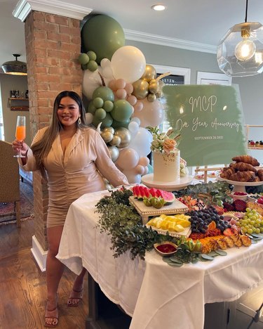 Woman holding champagne glass next to table of charcuterie and cake