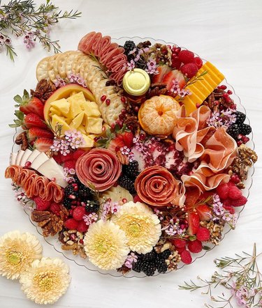 Charcuterie board with berries, salami roses, oranges, cheese, nuts and real flowers