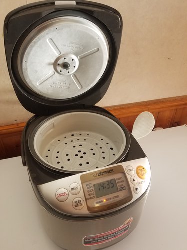 The author's rice cooker with the inner lid open, displaying the included steamer basket and rice paddle
