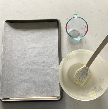 Sheet pan lined with parchment paper, bowl, and measuring cup