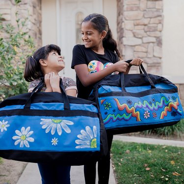 Two young children hold painted blue duffel bags