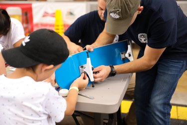A child and an older man assemble a blue skateboard