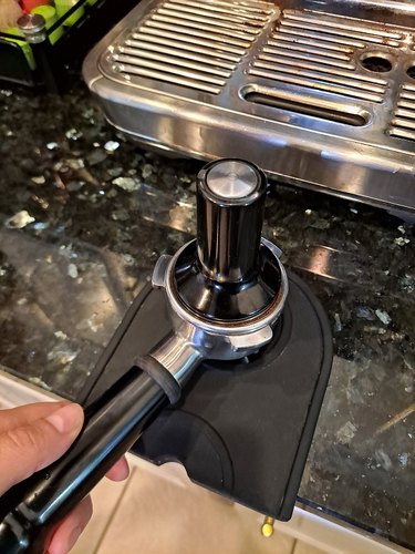 Tamping ground in a portafilter on top of a black silicone espresso tamper mat