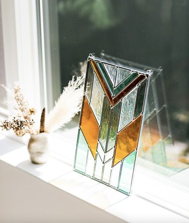 Rectangular stained glass piece with an art deco vibe leaning against a window to catch the light.