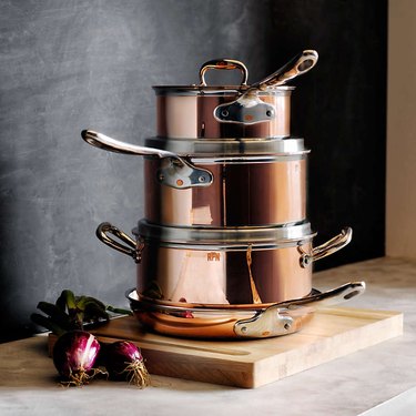 Stacked copper cookware on a cutting board, in front of a dark backsplash