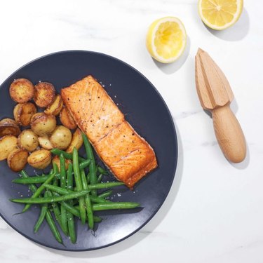 OXO citrus reamer and lemon halves alongside a plate of salmon and vegetables