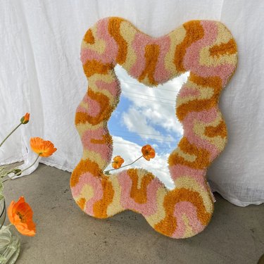 Hand-tufted wavy wall mirror in pink, cream, and orange hues.
