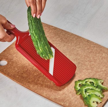 Red Kyocera slicer cutting a green vegetable on a cutting board.