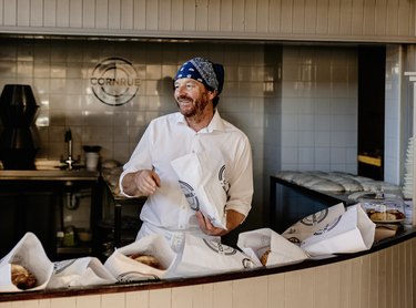 Man in blue bandana and white shirt places bread loaves into white paper bags