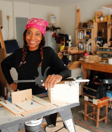 Smiling woman with pink bandana poses at a workbench