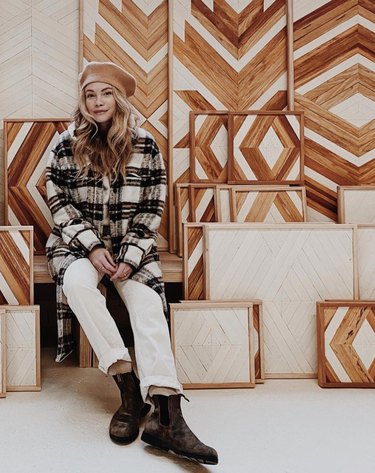 Woman sits next to a display of geometric wood art pieces.