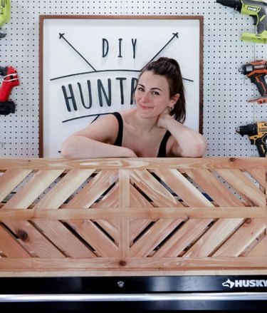 Woman posing with wooden headboard in front of sign reading "DIY Huntress"