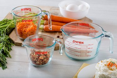 Pyrex measuring cups in multiple sizes, with ingredients and cutting board on a light countertop