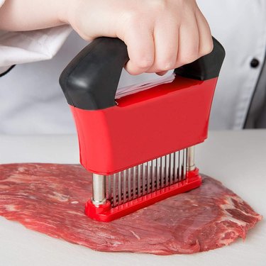 Black and red meat tenderizer in use on a piece of flank steak