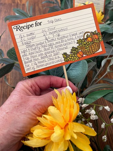 hand sticking wooden skewer with attached recipe card  into wreath form