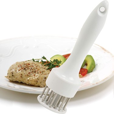 Compact Norpro meat tenderizer in front of a plate of chicken breast and vegetables