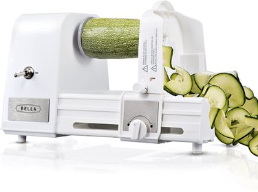 Electric Bella spiralizer cutting a zucchini, on a white ground