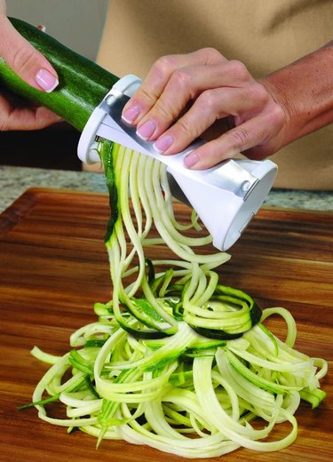 Handheld spiralizer cutting spirals of zucchini onto a wooden cutting board