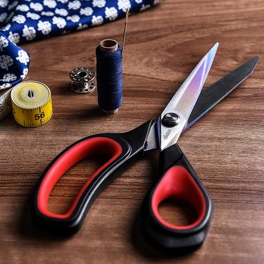 Livingo Tailor's scissors on a wooden desk next to thread and measuring tape