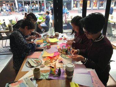 Four people seated around table folding colorful origami paper