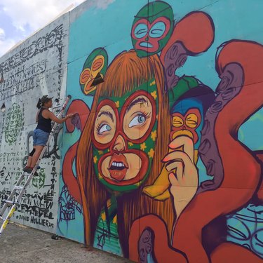 Person wearing denim shorts and black tank top spray-paints a bright mural