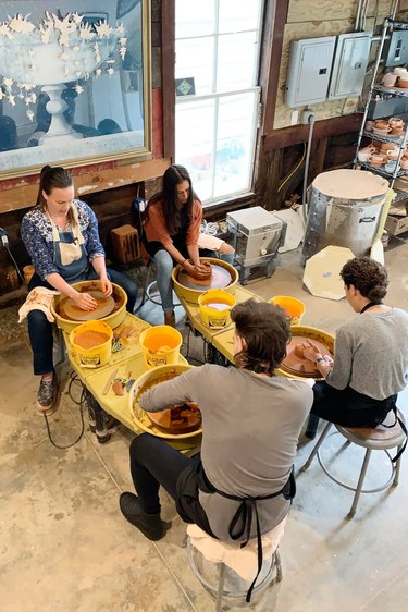 Four people sit around pottery wheels working with brown clay
