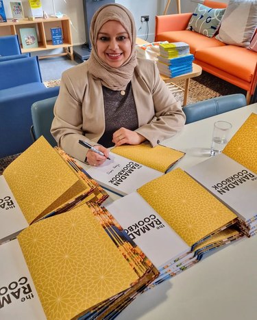 Woman wearing tan hijab signs copies of "The Ramadan Cookbook"