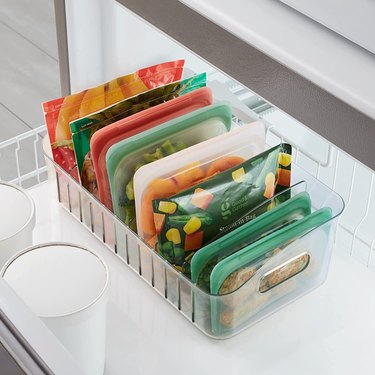 Clear plastic freezer organizer with 6 dividers for storing bags of frozen fruits or vegetables upright.