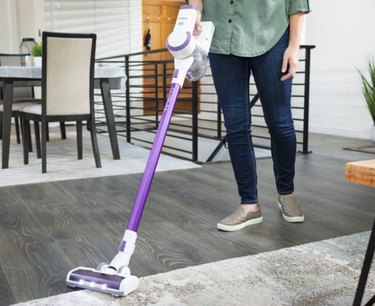 Woman using a Tineco A10-D in a living room with hardwood floors and carpet.