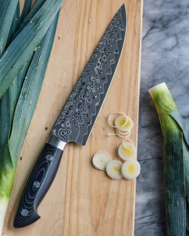 Kramer by Zwilling chef knife with Damascened blade, pictured on a wooden cutting board with sliced leeks
