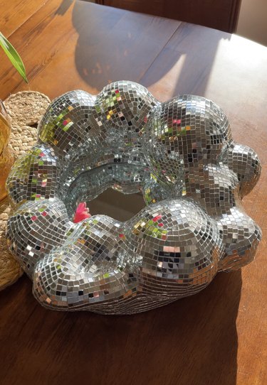 A round sculptural mirror covered in disco ball tiles