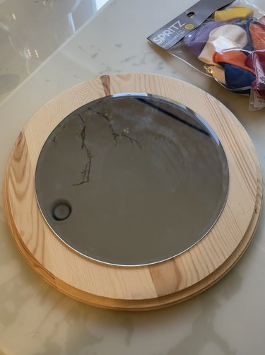 A round craft mirror on top of a round piece of wood.
