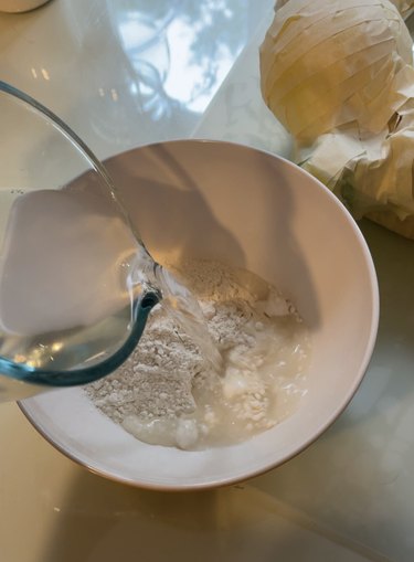 A bowl of flour with water pouring into it