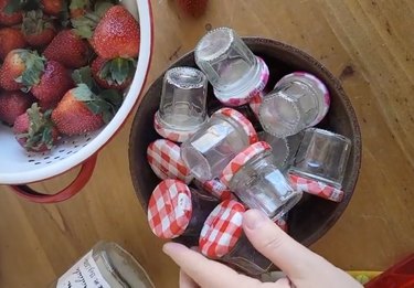 Bowl full of small empty jam jars next to a colander of fresh strawberries