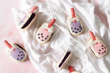 Finished boba-themed macarons on a white dishcloth over pink backdrop.