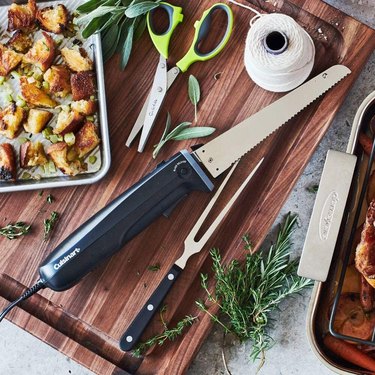 Electric knife on a wooden cutting board surrounded by ingredients.