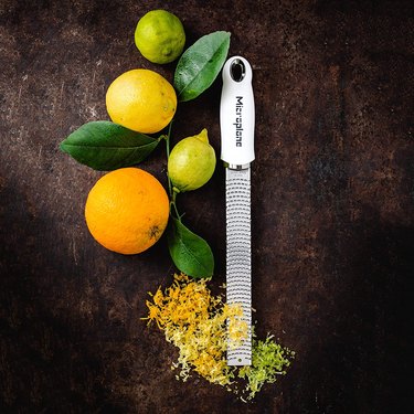 A Microplane Zester Grater surrounded by citrus fruits and zest