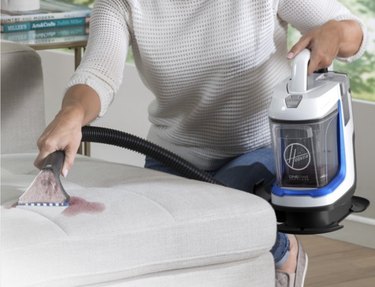 a woman in a white sweater holding a handheld, cordless vacuum,