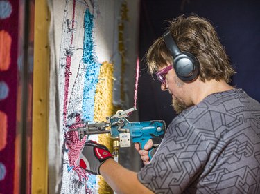 Tim, wearing headphones and gloves, uses a tufting gun to create a tufted piece of art.