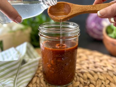Pour white vinegar into chili powder dye in a glass jar