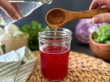 White vinegar getting poured into cranberry dye in a jar