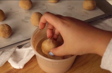 Rolling cookie dough balls in cinnamon sugar.