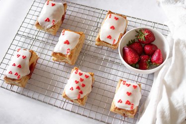 Playing card tarts filled with strawberry jam on a wire rack next to a bowl of strawberries