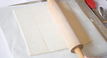 Thawed puff pastry sheet on work surface with rolling pin on top