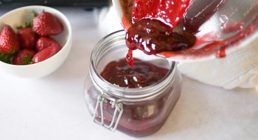 Pouring homemade strawberry jam into a jar