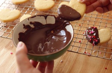 Scraping excess chocolate off shortbread cookie on rim of bowl.