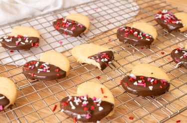 Heart-shaped shortbread cookies dipped in chocolate, arranged on a wire rack.
